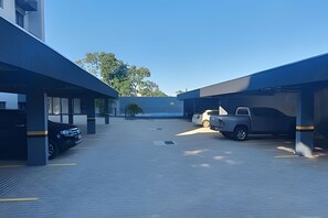 A parking area with two buildings, one with a covered section and another with a flat roof. - Residencial HS (Foz do Iguacu)
