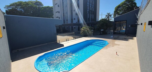 A swimming pool with a clear blue water surface, surrounded by a concrete deck and a low wall.