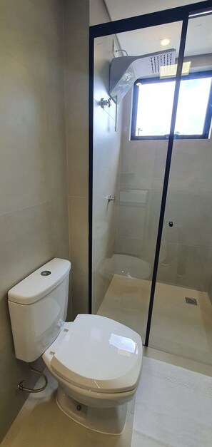 A bathroom with a toilet, a glass-enclosed shower, and a window.