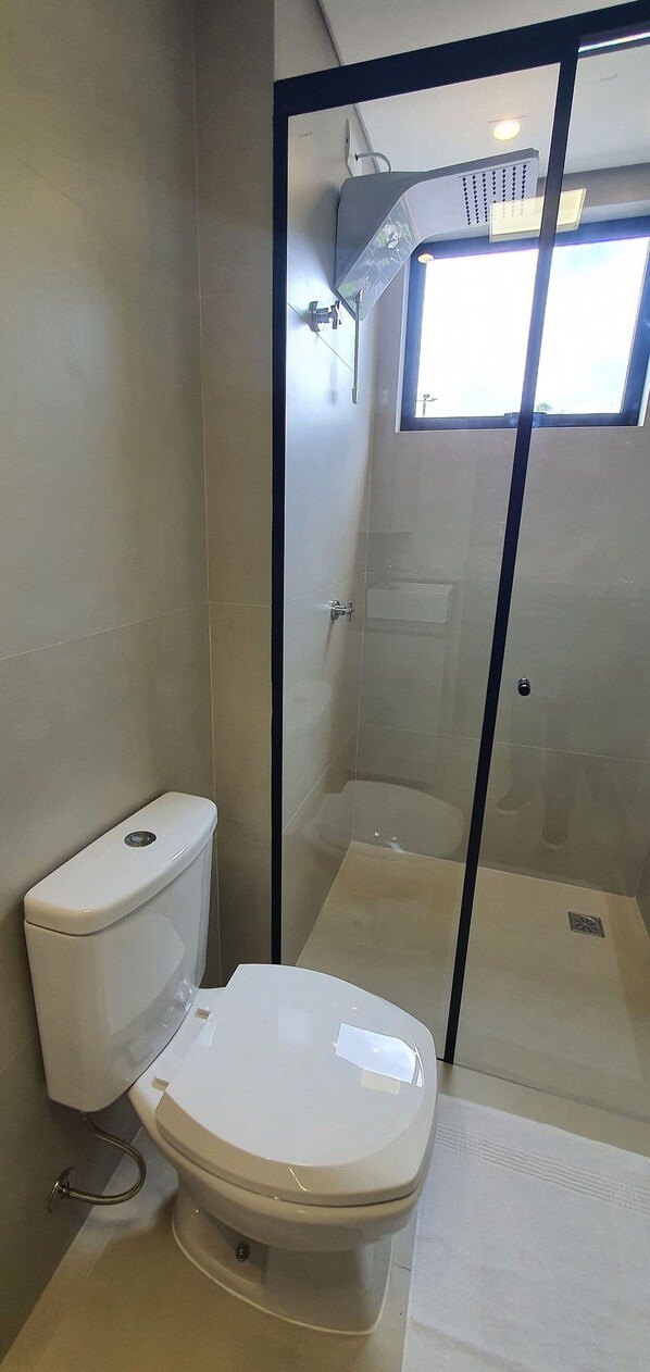 Une salle de bain avec des toilettes, une douche fermée par une paroi de verre et une fenêtre.