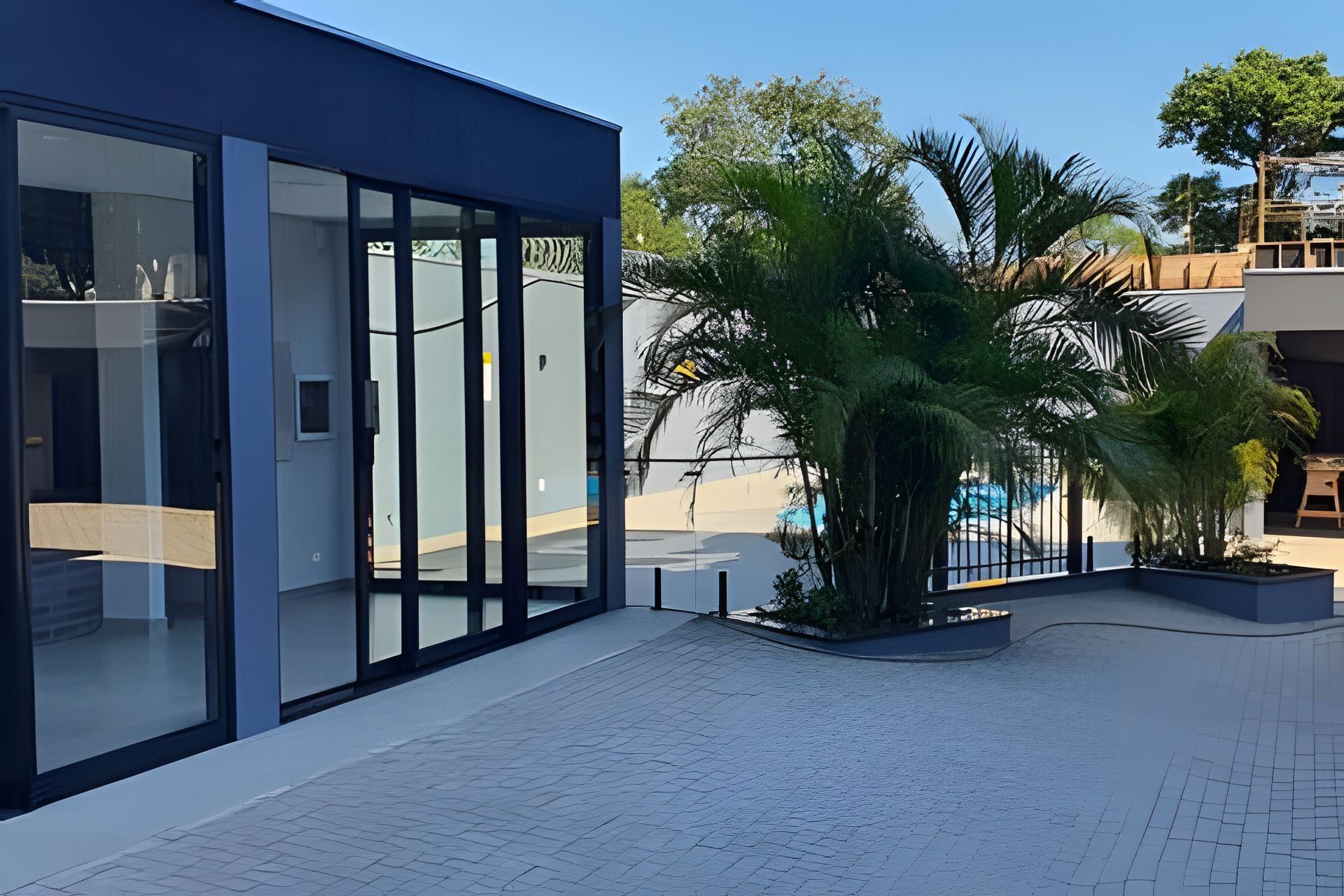 A modern building with large glass windows, a paved courtyard, and a palm tree.