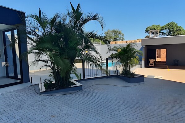 A modern outdoor patio with a pool, surrounded by palm trees and a clear sky.