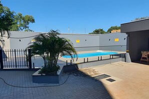 Une piscine avec une terrasse carrelée, un palmier et une clôture.