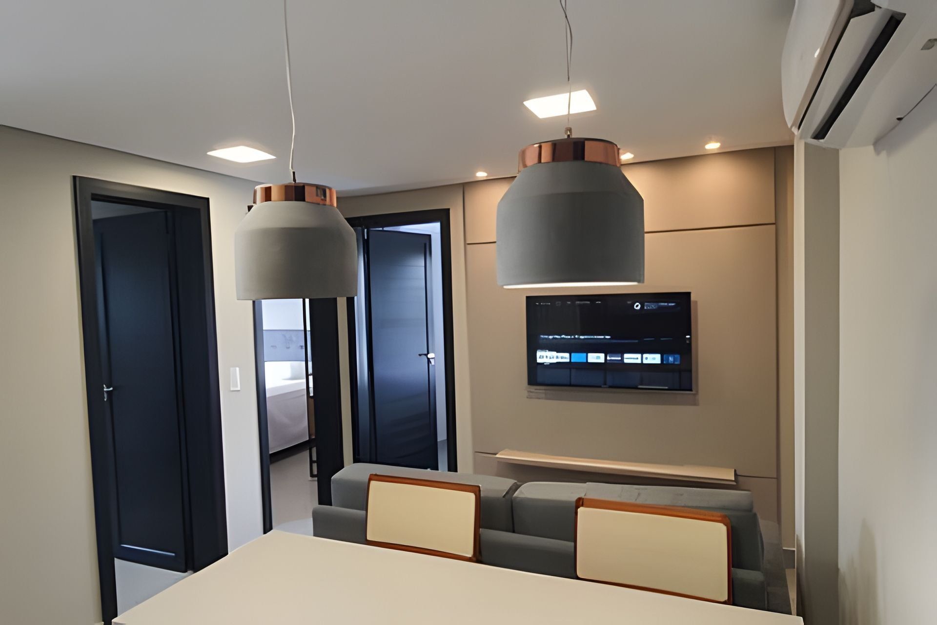 Uma sala de conferências moderna com uma mesa comprida, duas cadeiras, uma TV montada e iluminação pendente.