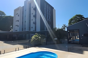 A modern building with a pool area, including a clear sky and some greenery. - Residencial HS (Foz do Iguacu)