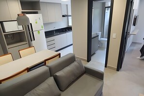 Une cuisine moderne avec des armoires blanches, un comptoir noir et un four encastré. On y trouve un coin repas avec une table et des chaises, ainsi qu’un canapé gris.