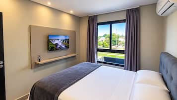 Quarto de hotel com cama, TV montada na parede, janela com cortinas e ar condicionado.