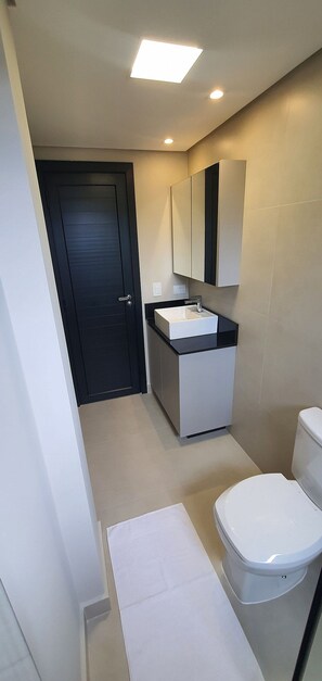Ein modernes Badezimmer mit einer dunklen Tür, einem weißen Waschbecken mit schwarzer Arbeitsplatte, einem Spiegel über dem Waschbecken und einer weißen Toilette.