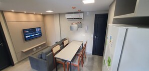 Une cuisine moderne équipée d’un four encastré, d’un réfrigérateur, d’une table à manger avec des chaises, d’un téléviseur fixé au mur et d’un petit coin salon avec des coussins.