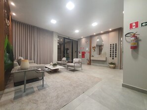 A modern hotel lobby with a seating area, a reception desk, and a fire extinguisher on the wall. - Residencial HS (Foz do Iguacu)