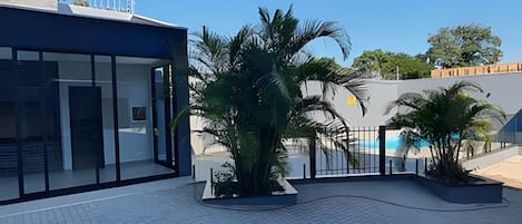 A modern building with a glass facade, a paved courtyard, and palm trees.