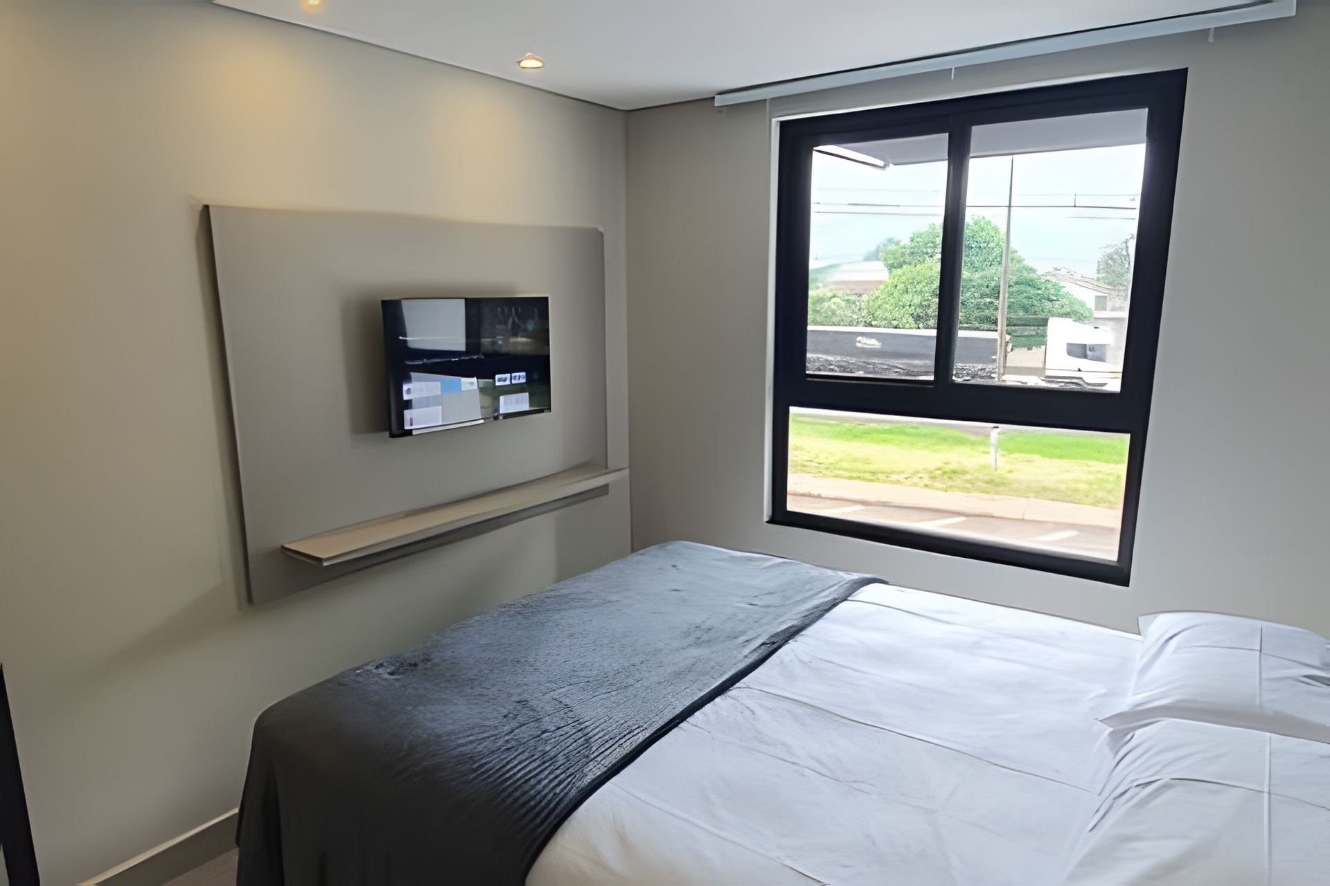 Un dormitorio con cama, televisor montado en la pared y ventana con vistas al exterior.