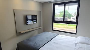 Un dormitorio con cama, televisor montado en la pared y ventana con vistas al exterior.