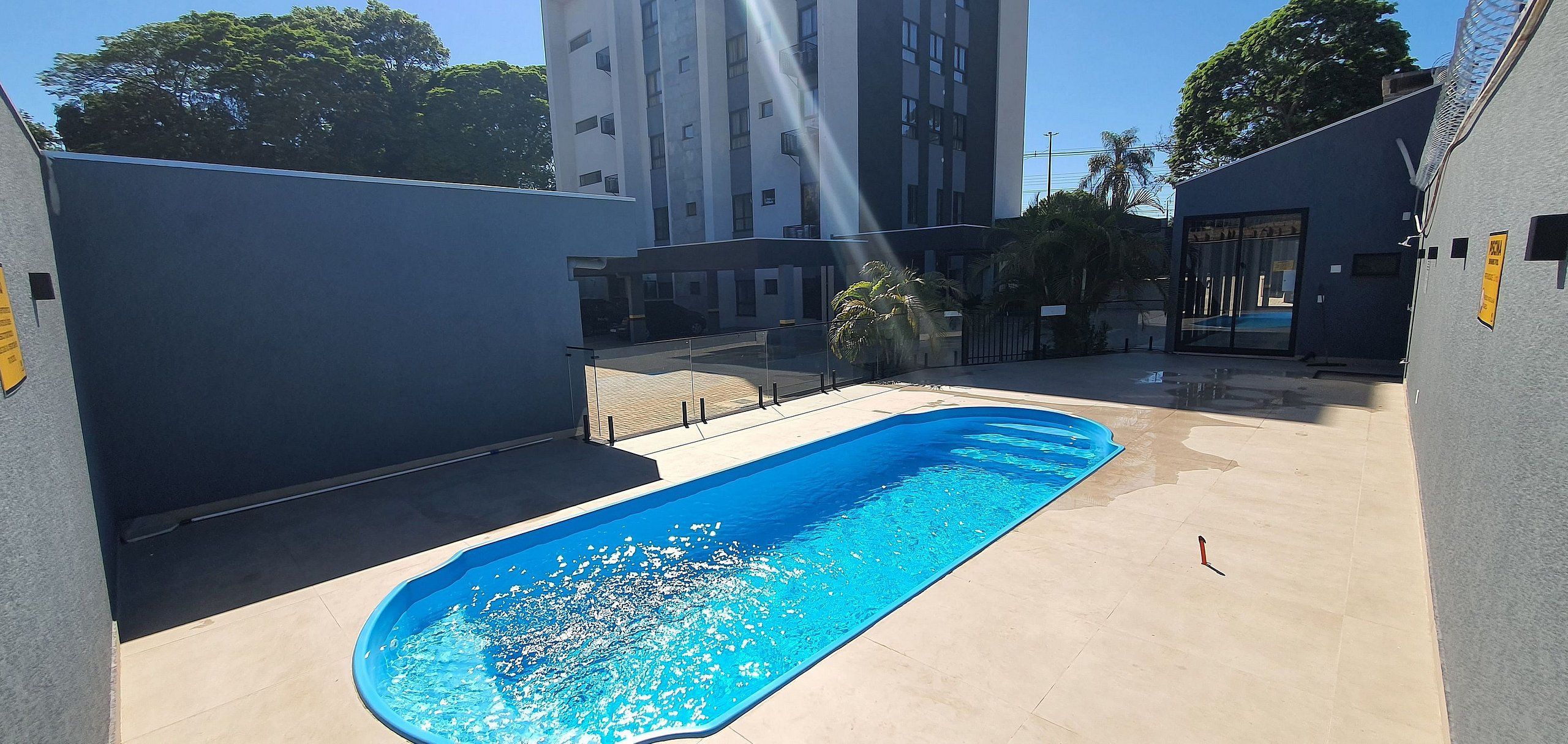 A swimming pool with a clear blue water surface, surrounded by a concrete deck and a low wall.