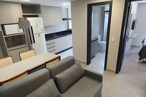 A modern kitchen with white cabinets, a dining area with a table and chairs, and a view into the bathroom through an open doorway. - Residencial HS (Foz do Iguacu)
