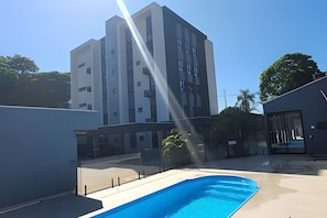 A modern building with a swimming pool, surrounded by a fence and greenery. - Residencial HS (Foz do Iguacu)