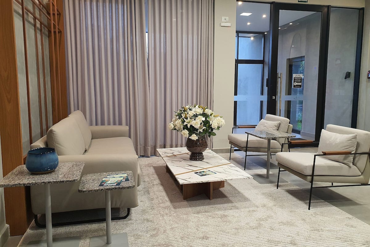 A modern hotel lobby with a sofa, armchairs, a coffee table, and a vase of flowers.