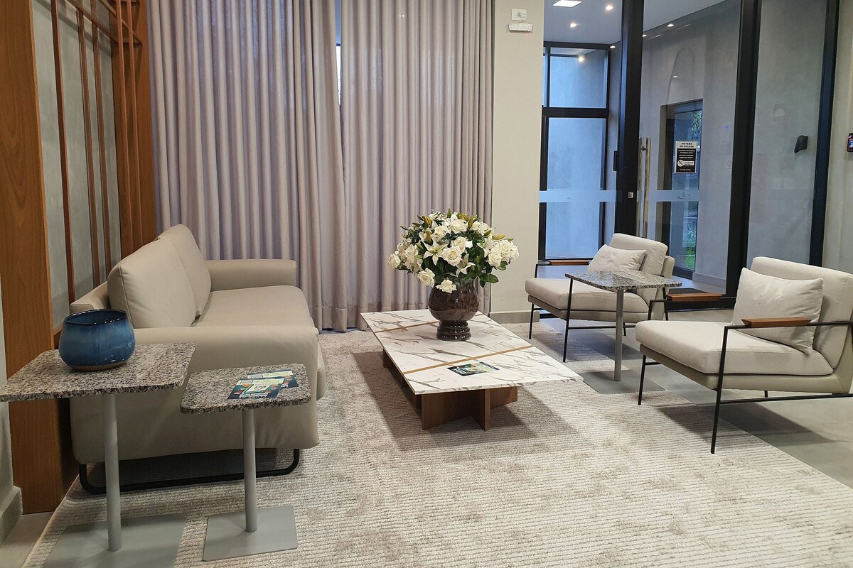 Un moderno vestíbulo de hotel con un sofá, sillones, una mesa de centro y un jarrón con flores.