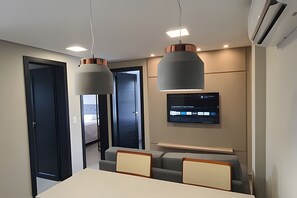 A modern conference room with a long table, two chairs, a mounted TV, and pendant lighting. - Residencial HS (Foz do Iguacu)