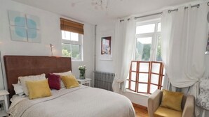 A bedroom with a large bed, a wooden floor, a chair, a radiator, and a window with curtains. - Charming 3 Bed Home with Garden & Parking near Worcester (Lower Broadheath)