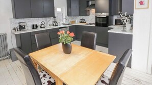 A modern kitchen with dark cabinets, a wooden dining table, and a vase of flowers. - Charming 3 Bed Home with Garden & Parking near Worcester (Lower Broadheath)
