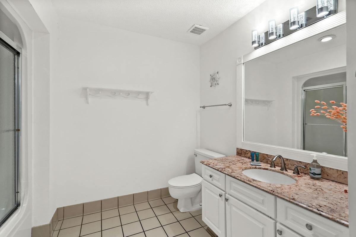 A bathroom with a white toilet, a sink with a marble countertop, and a large mirror above the sink.