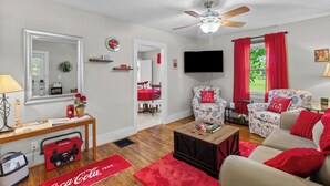 Una sala de estar con ventilador de techo, televisor, cortinas rojas y un sofá.