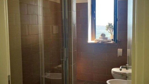 Un baño con mampara de vidrio, una ventana con vistas y un lavabo.