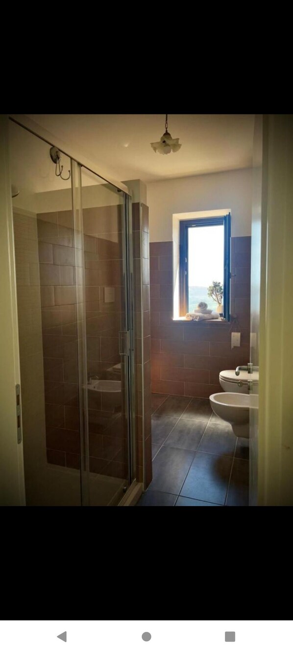 A bathroom with a glass shower door, a window with a view, and a sink.