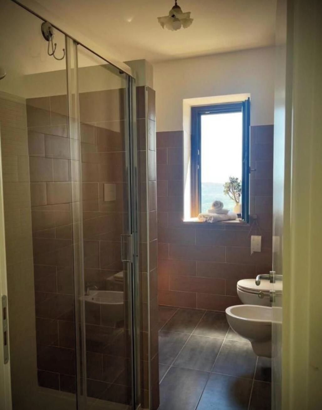 A bathroom with a glass shower door, a window with a view, and a sink.