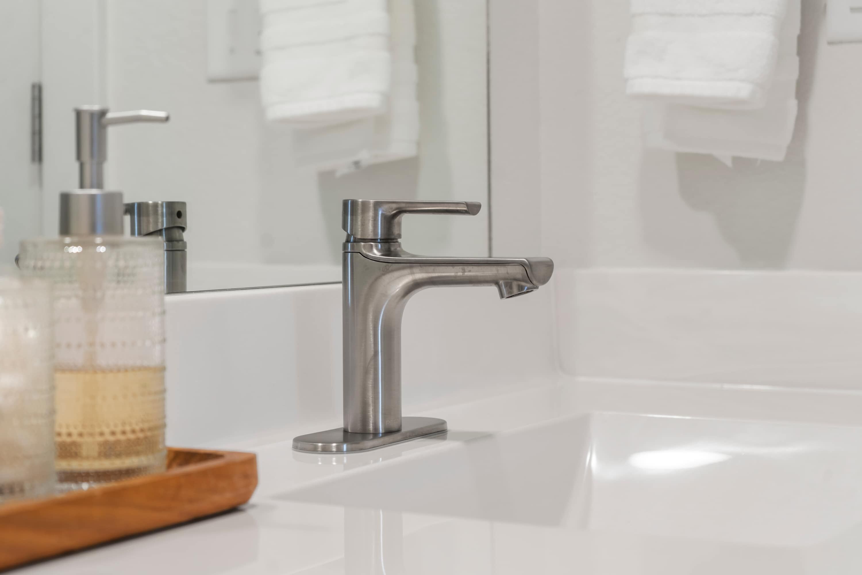 A modern bathroom with a chrome faucet, a glass soap dispenser, and a wooden tray.