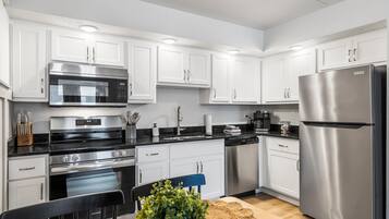 A modern kitchen with white cabinets, stainless steel appliances, and a wooden dining table with a plant and cookies.