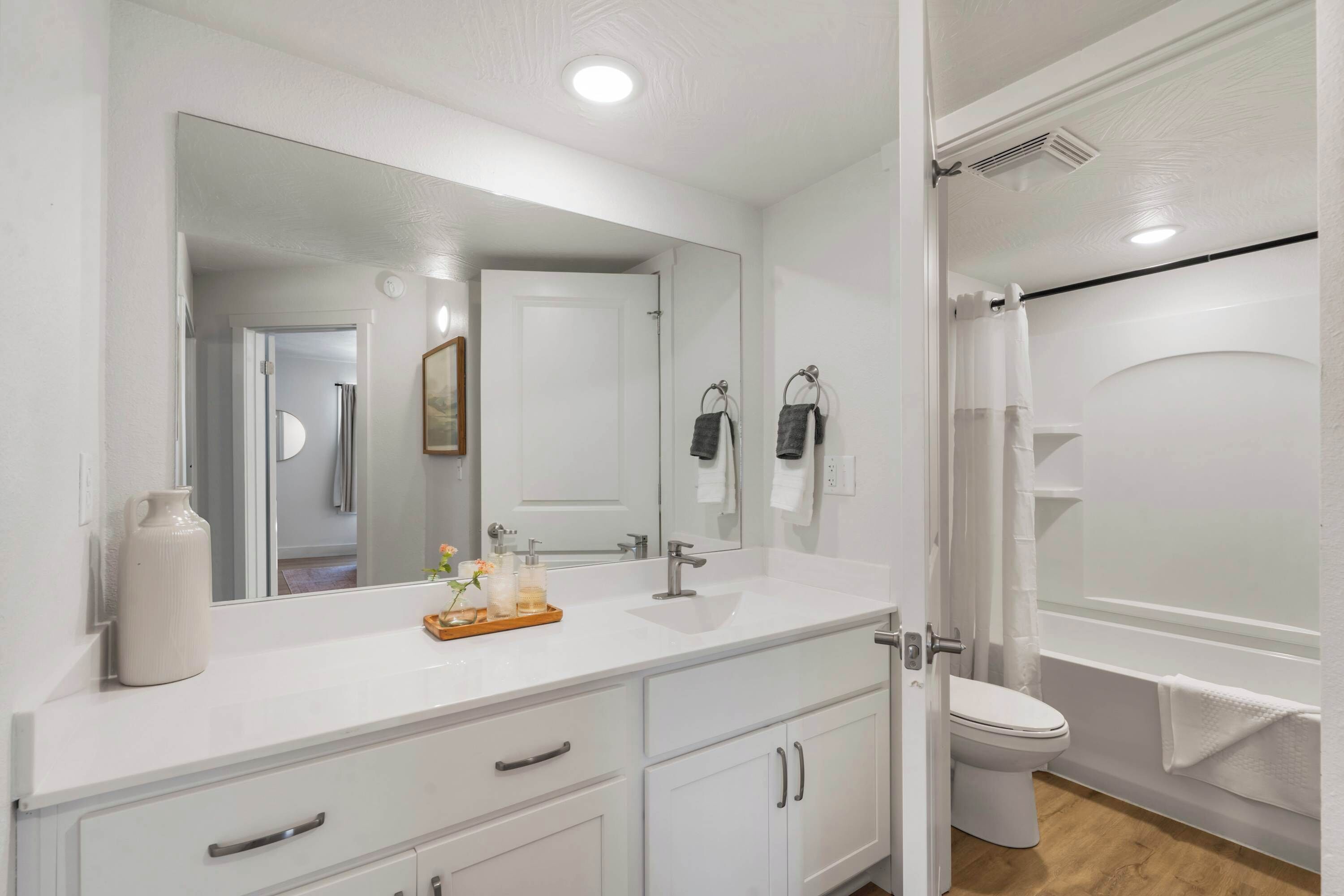 Un baño moderno con tocador blanco, un espejo grande, inodoro y zona de ducha.