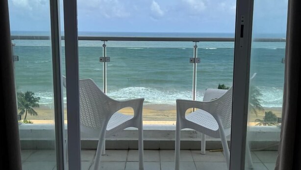 A balcony with two white plastic chairs facing a beach and ocean view. - Blue Ocean Apartment by EPICK (Dehiwala-Mount Lavinia)