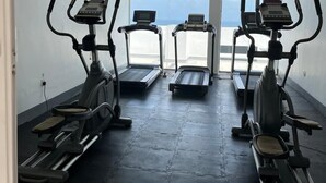 A gym with four treadmills and two elliptical machines, large windows, and a ceiling fan. - Blue Ocean Apartment by EPICK (Dehiwala-Mount Lavinia)
