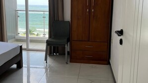 A hotel room with a bed, a chair, a wardrobe, and a view of the ocean through a sliding door. - Blue Ocean Apartment by EPICK (Dehiwala-Mount Lavinia)