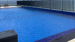 A swimming pool with a black railing, a tiled deck, and a clear sky. - Blue Ocean Apartment by EPICK (Dehiwala-Mount Lavinia)