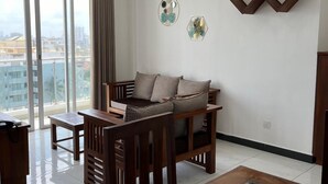 A modern living room with a glass coffee table, wooden furniture, and decorative wall art. - Blue Ocean Apartment by EPICK (Dehiwala-Mount Lavinia)