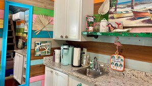 A kitchen with a sink, cabinets, and a painting of a beach scene. - Perdido Surf Shack-tiny home on a hobby farm close to Perdido Key Beach and NAS (Pensacola)