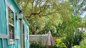 A turquoise house with a 'hello' mat at the entrance, a garden with mulch, and a wooden fence. - Perdido Surf Shack-tiny home on a hobby farm close to Perdido Key Beach and NAS (Pensacola)