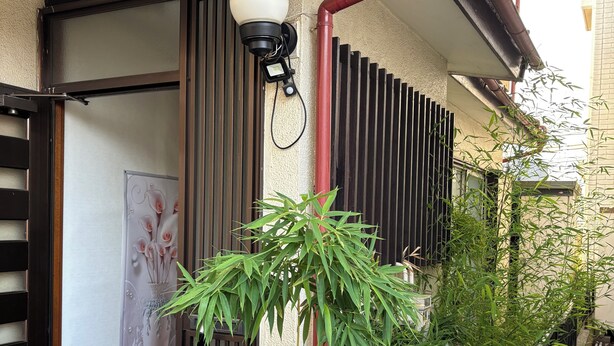Un immeuble résidentiel doté d’une porte coulissante, d’une caméra de surveillance, d’un pot de fleurs et de deux bouteilles de gaz.