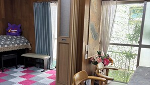 Une pièce avec un plancher en bois, un lit recouvert d’une couvre-lit à motifs, un bureau, une chaise et une fenêtre donnant sur un paysage verdoyant.
