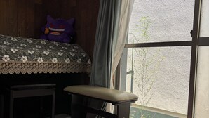 Une chambre avec un lit, un banc, une fenêtre avec des rideaux et une vue sur la verdure à l’extérieur.