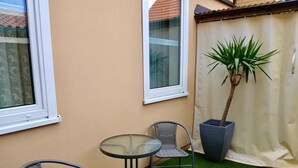 A small patio area with two wicker chairs and a glass table, a potted plant, and a curtain. - Vacation apartment König (Arendsee)
