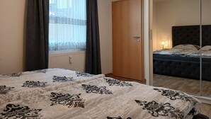 A bedroom with a large bed, a wardrobe, a mirror, and a window with curtains. - Vacation apartment König (Arendsee)