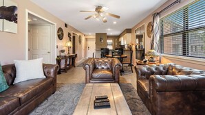 A spacious living room with leather sofas, a coffee table, and a ceiling fan.