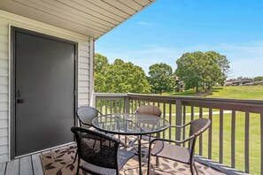 Une terrasse couverte avec une table et des chaises, une porte et une vue sur une pelouse verdoyante et des arbres.