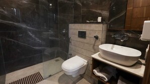 Un baño moderno con ducha acristalada, inodoro blanco y un lavabo ovalado grande.