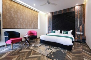 A modern hotel room with a large bed, a desk, two chairs, and a patterned wall.