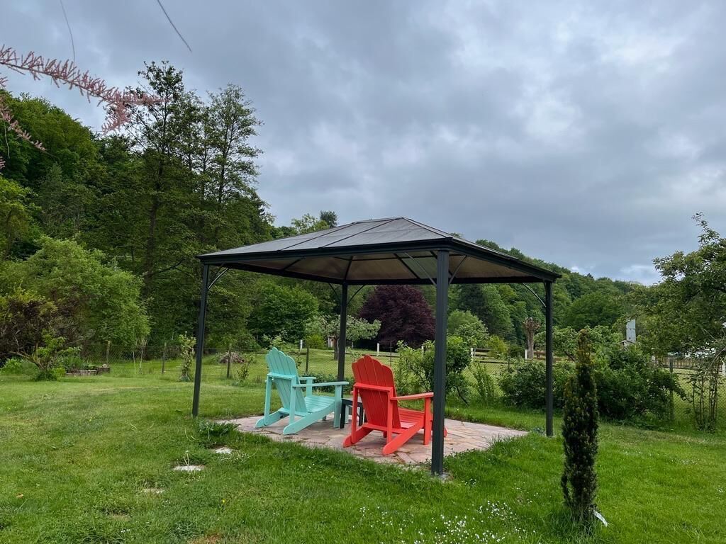 Un kiosque doté d’un toit, entouré de verdure, d’herbe et d’arbres.